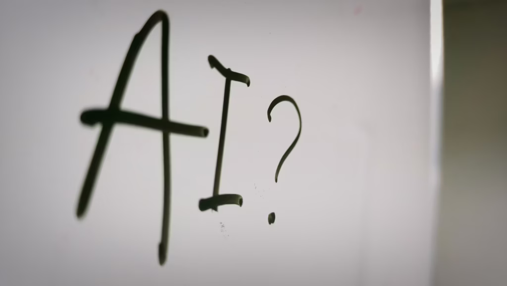The words AI followed by a question mark written on a whiteboard in black ink marker