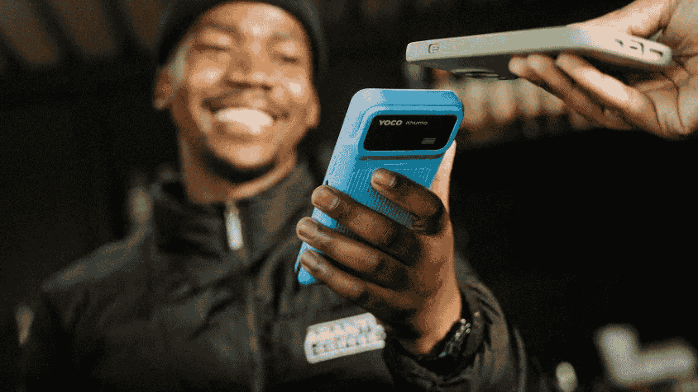 Close-up of a smiling man holding a blue Yoco Khumo card reader, tapping it against another handheld payment device.