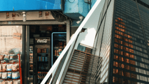 A diagonal split image with a township spaza shop front on the left and glass office towers photographed from below on the right.